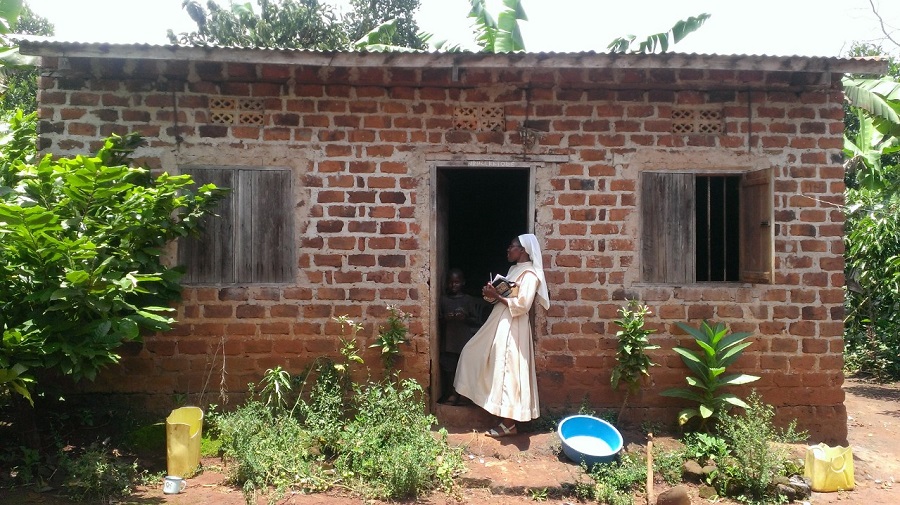Sr. Carolyne, CARITAS For Children Program Coordinator in Uganda, approaches the family home of hand-made, red bricks in Maseke