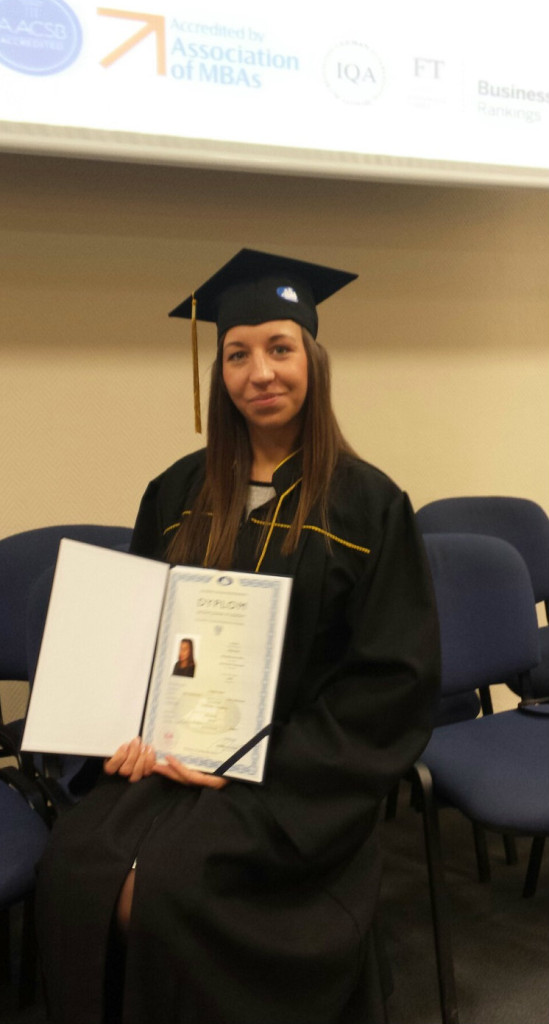 Young woman sitting, dressed in graduation cap and gown holding diploma.