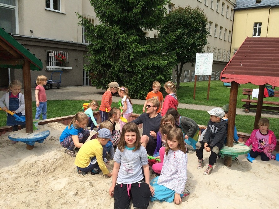 image of young man surrounded by children in sandbox
